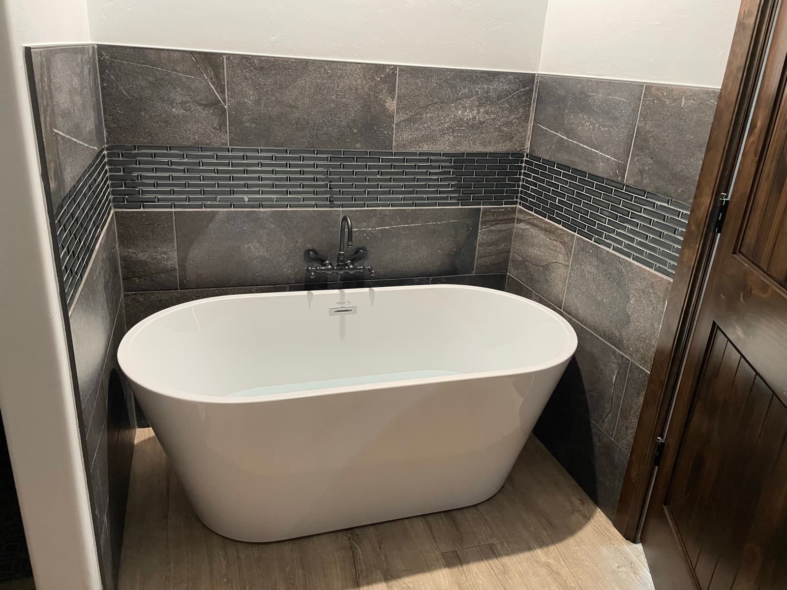 A finished freestanding bathtub installation with dark tile and modern trim.