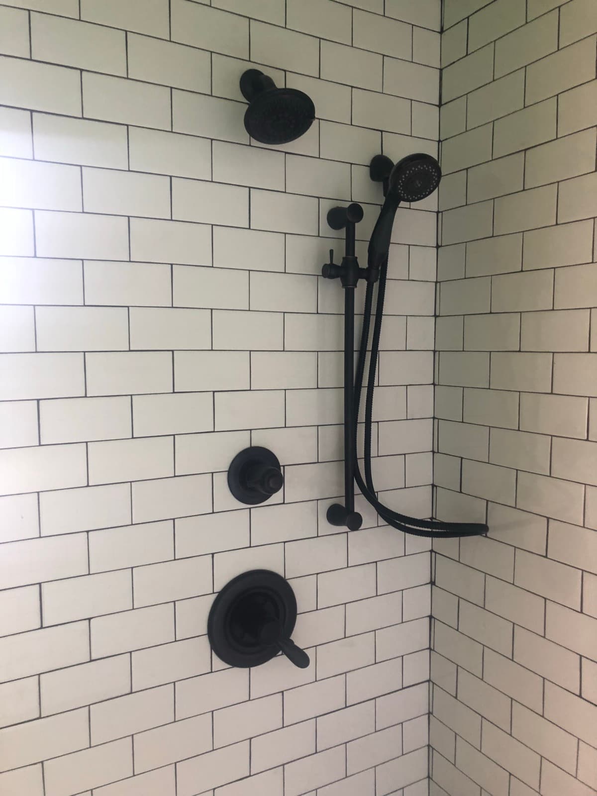 Matte black shower fixtures installed on white tile.